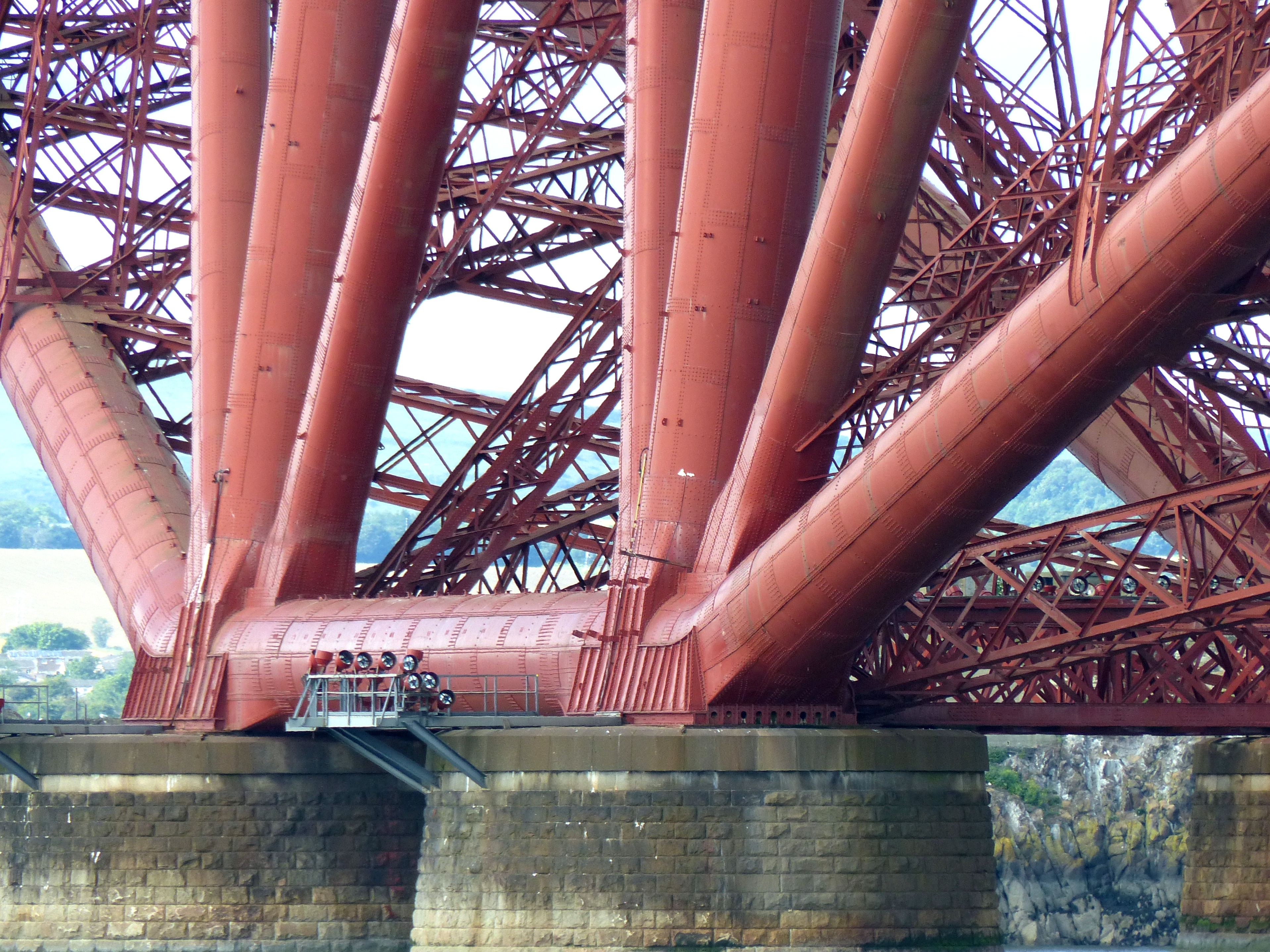 A close-up view of the Forth Bridge's steel cantilever structure, showing the tubular lattice towers and the crossed diagonal bracing of the anchor and cantilever arms