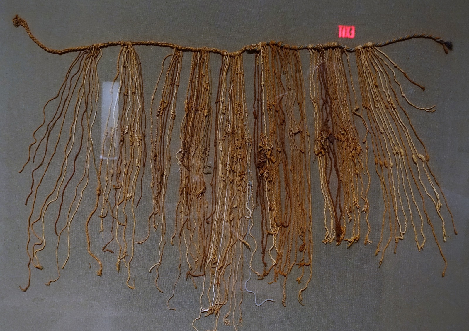 A fragmentary Inca quipu from the Late Horizon period, showing a thick horizontal main cord with dozens of thinner knotted pendant cords hanging from it in varied natural fiber colors